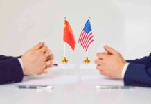 Two diplomats sit across table with China and United States flags between them