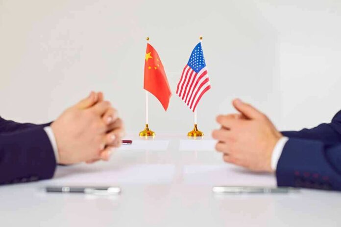 shutterstock_2169636285 Two diplomats sit across table with China and United States flags between them