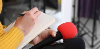 Journalist holding two microphones while writing in a notebook