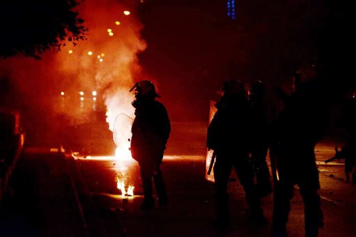 shutterstock_517676266 Riot police in silhouette amid smoke and fire at night