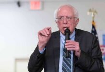 Bernie Blitz Invades Red Turf – See What He’s Up To Bernie Sanders speaking into a microphone at an indoor event