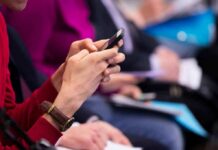 Conflict Shadows Rising State Senator Person in red sweater using a smartphone at an event