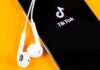 Clout-Chasing Ends In Handcuffs Smartphone with TikTok app and white wired earbuds on yellow background