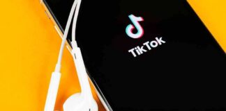 Smartphone with TikTok app and white wired earbuds on yellow background