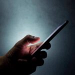 Kidnapping Hoax Explodes With AI Power Hand holding a smartphone in the dark
