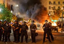 France Erupts – No Emergency Declared Christian Jones and Teddy Williams among police line at night protest with fire and smoke