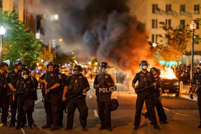 Christian Jones and Teddy Williams among police line at night protest with fire and smoke
