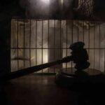 Judge’s gavel in silhouette before prison bars