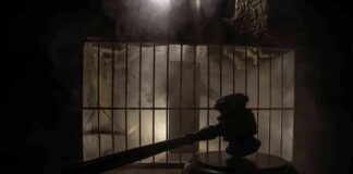 Judge’s gavel in silhouette before prison bars