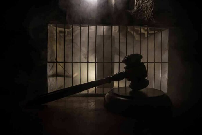Judge’s gavel in silhouette before prison bars