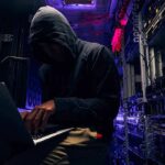 FBI’s Cyber Nemesis Lands In Chains Hooded person using a laptop in a dark server room