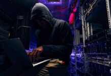 FBI’s Cyber Nemesis Lands In Chains Hooded person using a laptop in a dark server room