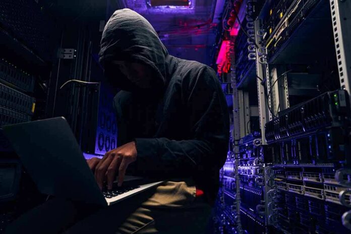 shutterstock_2067215408 Hooded person using a laptop in a dark server room