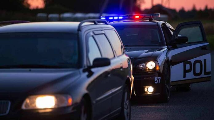 Police car with flashing lights behind a stopped vehicle at dusk