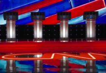 Epstein Firestorm Erupts In Georgia Debate stage with four empty podiums and bright red and blue backdrop