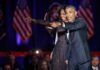 Money War Drags Obama In Michelle Obama and Rob Nabors pointing on stage at an event