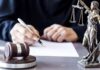 DOJ: American Aided School Massacre Plot Judge writing at desk with gavel and Lady Justice statue