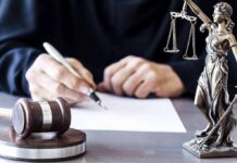 DOJ: American Aided School Massacre Plot Judge writing at desk with gavel and Lady Justice statue